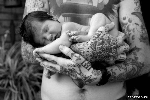 Папа с татуировками на руках держит ребенка